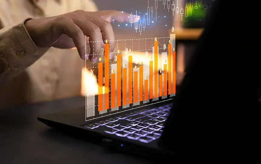 Pessoa interagindo com um laptop enquanto gráficos digitais em barras e velas são projetados sobre a tela, representando análise de indicadores de risco e dados financeiros