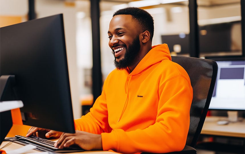 homem sorrindo de casaco na cor laranja e usando computador 