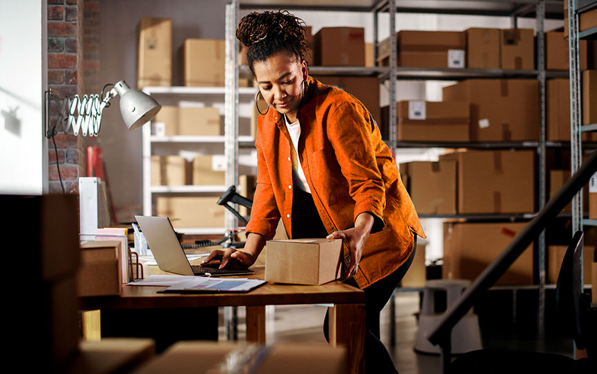 Empreendedora de e-commerce embalando pedido em estoque. Pequenos negócios da região Nordeste enfrentam desafios com fraudes e precisam de soluções antifraude eficazes.