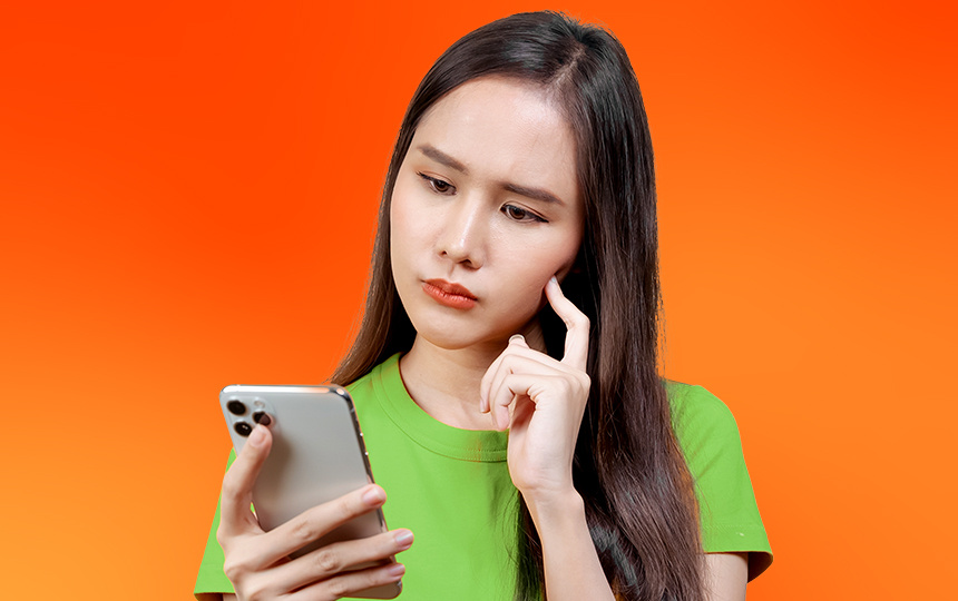 Menina asiática de cabelo escuro comprido segurando celular na mão e com semblante confuso